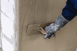 Construction worker holding plastering trowel smoothing wall defects