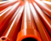Metallic Pipes Covered With Orange Paint. Background With Perspective. Selective Focus.
