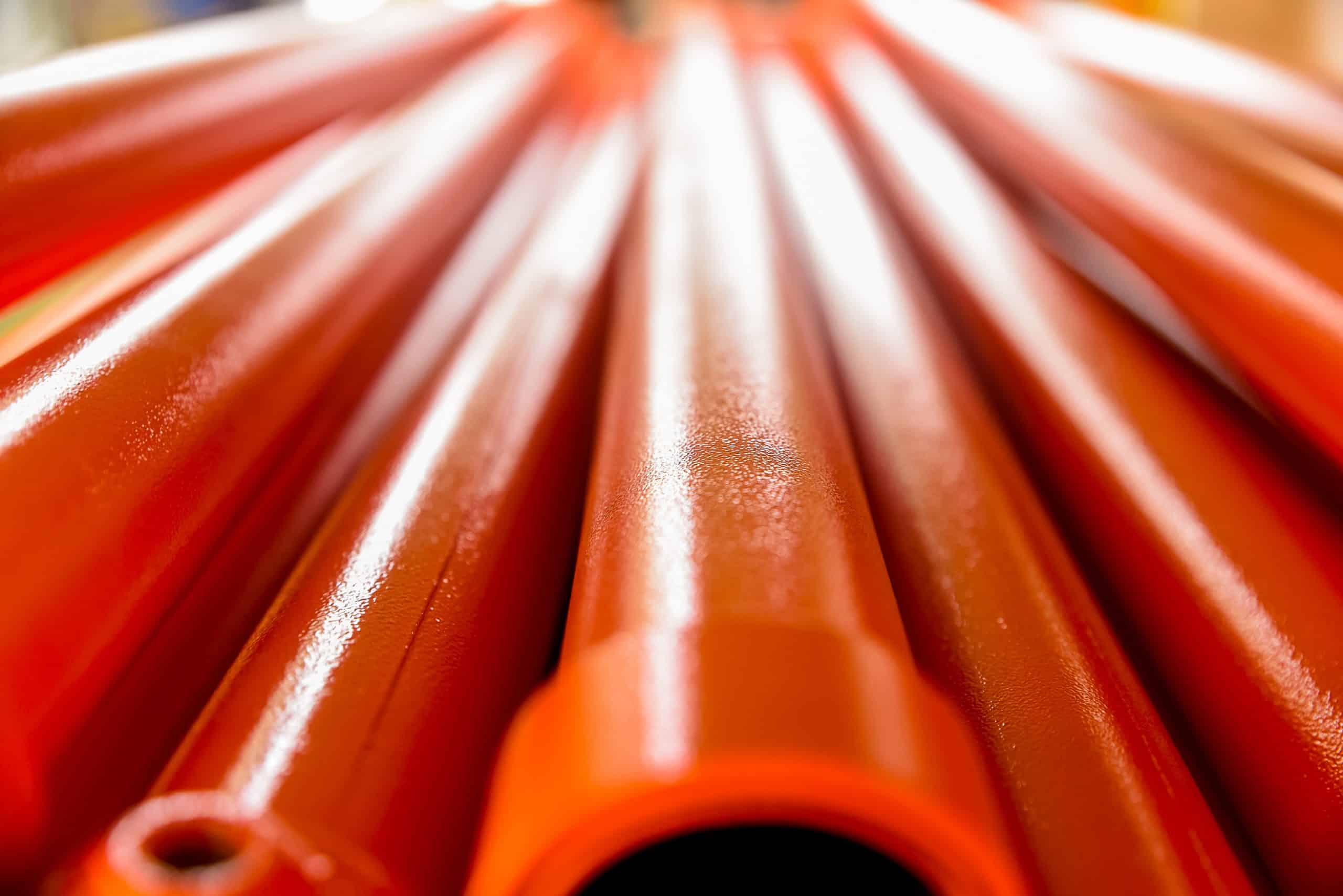 Metallic Pipes Covered With Orange Paint. Background With Perspective. Selective Focus.